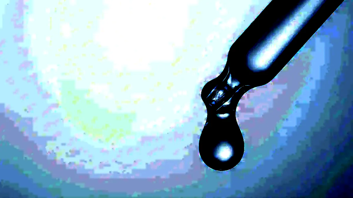 Macro photograph of a clear droplet hanging from the tip of a glass pipette.