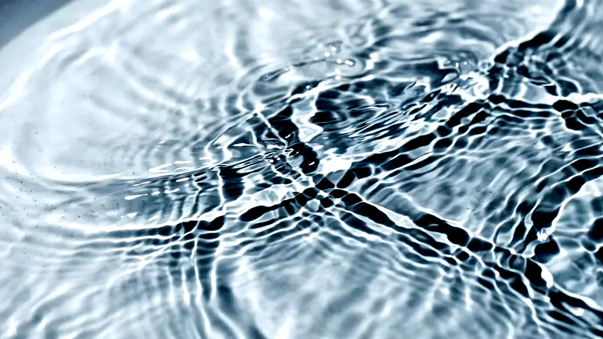 Rippling caustic light patterns cast through moving water onto a pale surface.
