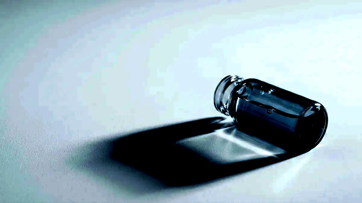 A single unlabelled glass vial lying on its side under raking light.