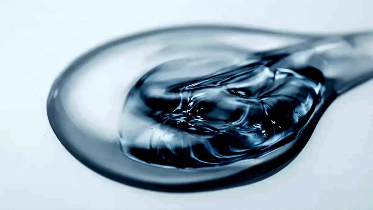 Extreme macro of a clear viscous serum pooled across a flawless white surface.