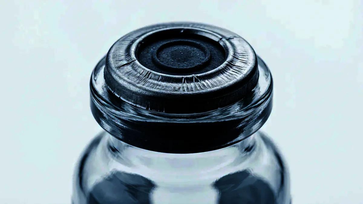 Extreme close-up of the stopper and crimped seal of an unlabelled glass vial.