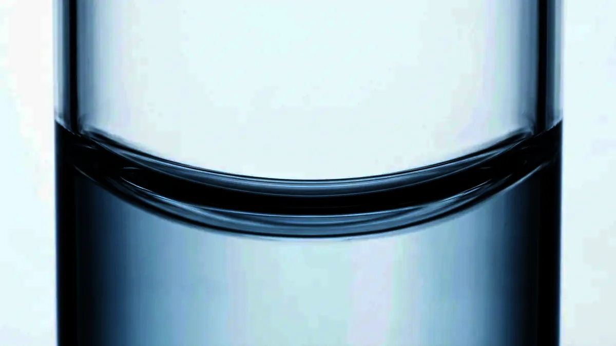 Macro photograph of the curved liquid surface inside a plain glass vessel.