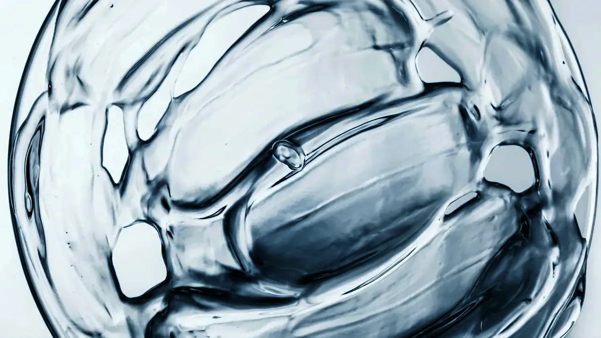 Overhead macro of clear gel spread thin across glass, light caught in its ridges.