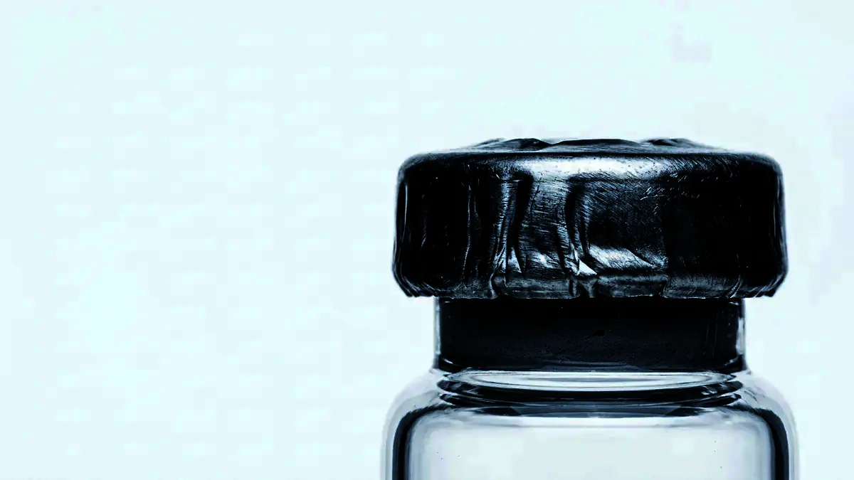 Extreme close-up of the crimped aluminium seal and grey stopper of a glass vial.