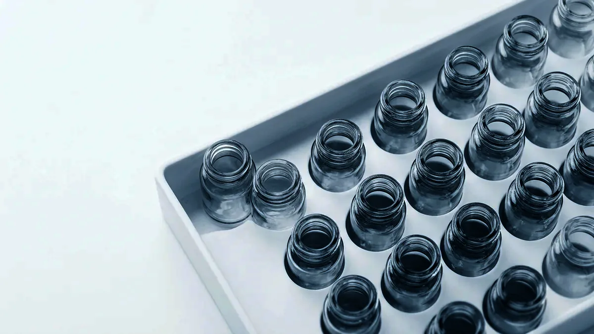 Overhead view of unlabelled glass vials standing evenly spaced in a white tray.