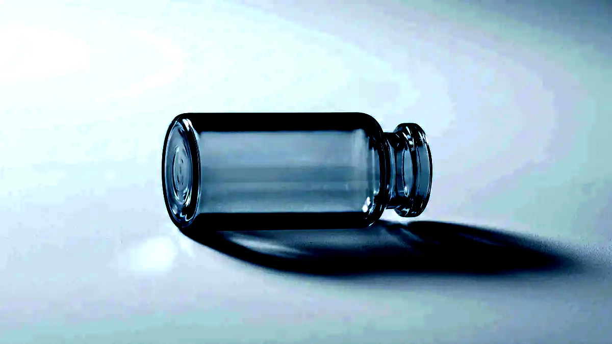 A single unlabelled glass vial lying on its side under raking light.