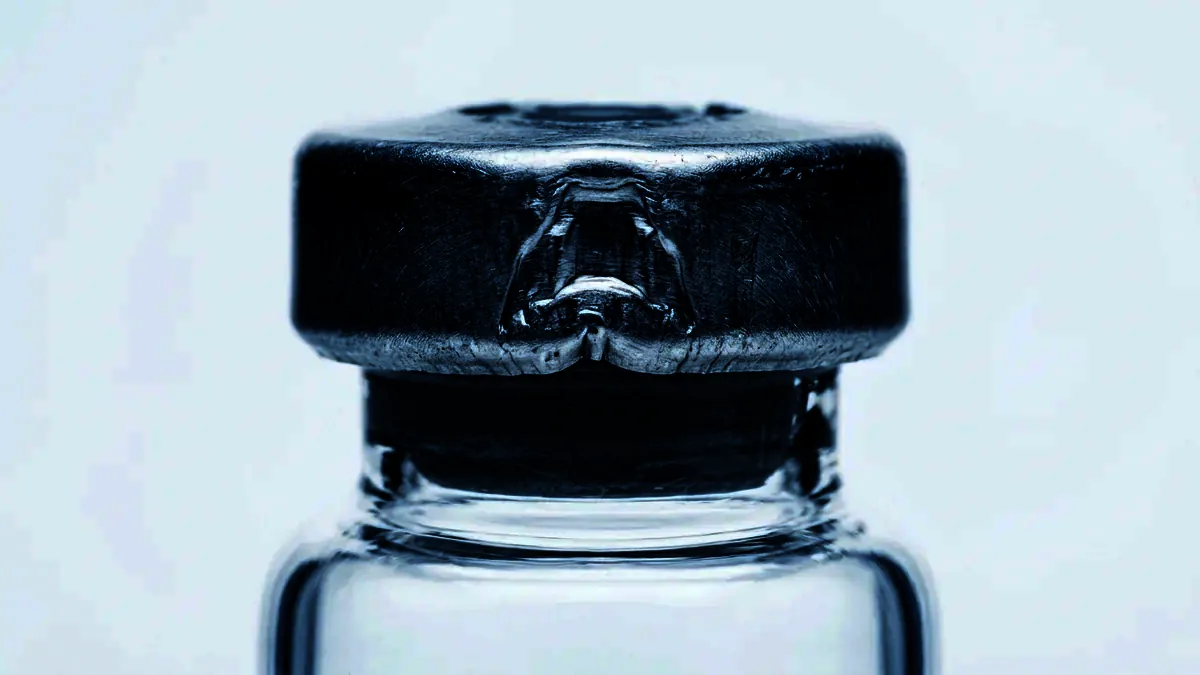 Extreme close-up of the crimped aluminium seal and grey stopper of a glass vial.
