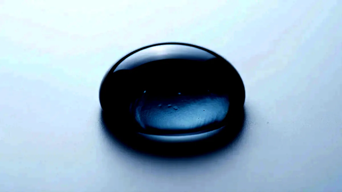 Extreme close-up of a bead of clear liquid resting on a flawless white surface.