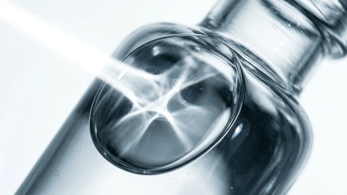 Macro of the shoulder of a plain glass vial refracting light into a bright caustic.